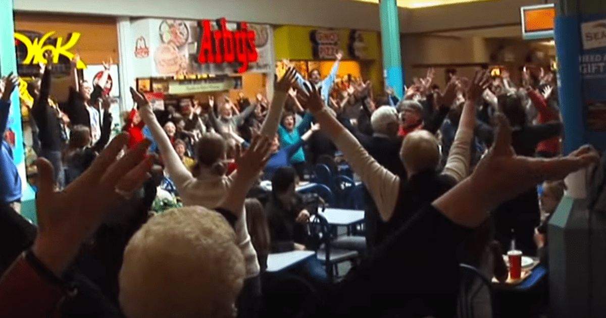 A large group of people in a restaurant raise their hands in the air, possibly cheering or celebrating.