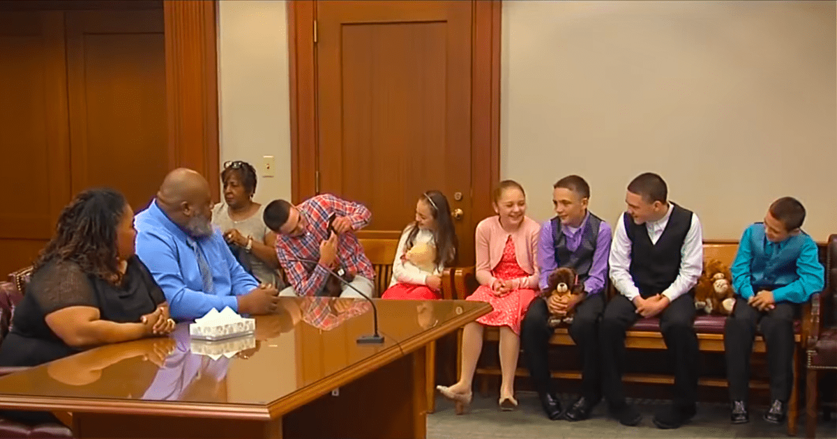 A group of people, including children and adults, are seated in a courtroom setting, appearing to be in a formal or legal...