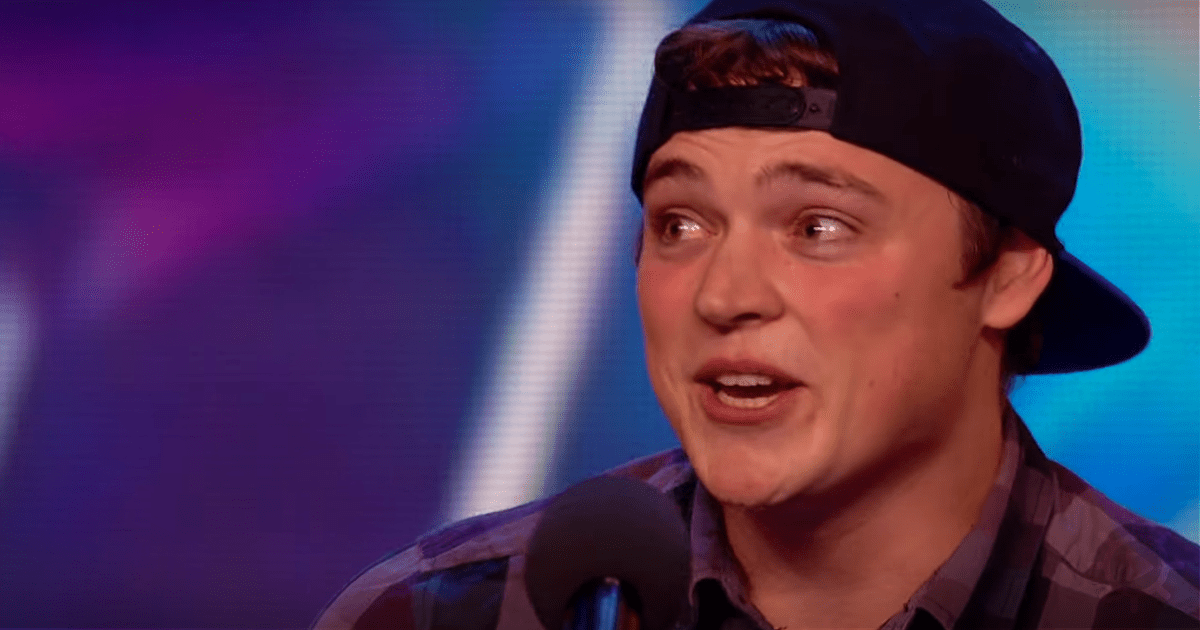 A person wearing a cap and plaid shirt speaks into a microphone against a colorful background.