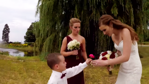 A bride in a white wedding dress is holding a bouquet of flowers, surrounded by bridesmaids in red dresses.