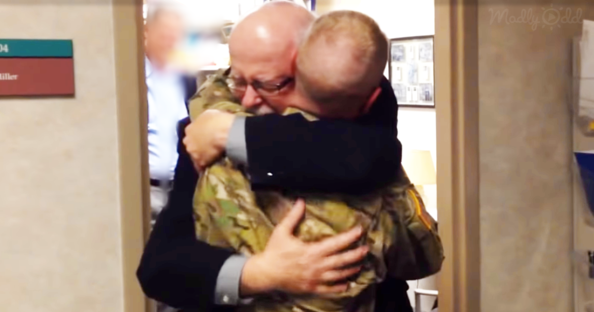 A man in a suit hugs another in camouflage, both appearing emotional, in a hallway.