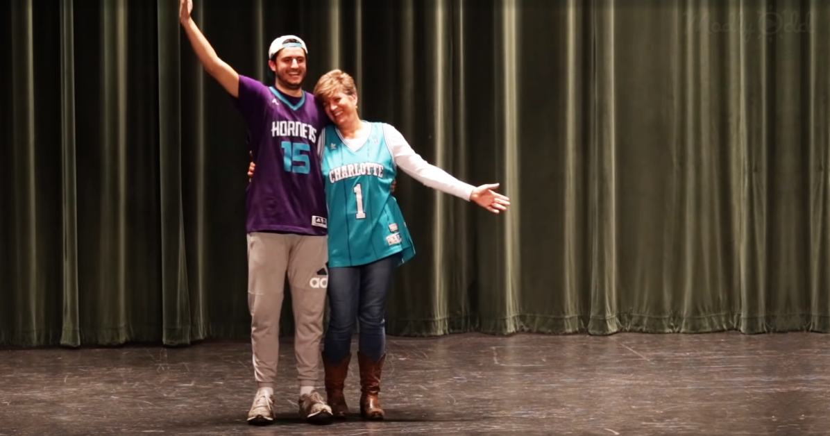 A man and woman in Hornets and Charlotte jerseys pose on stage with arms outstretched.