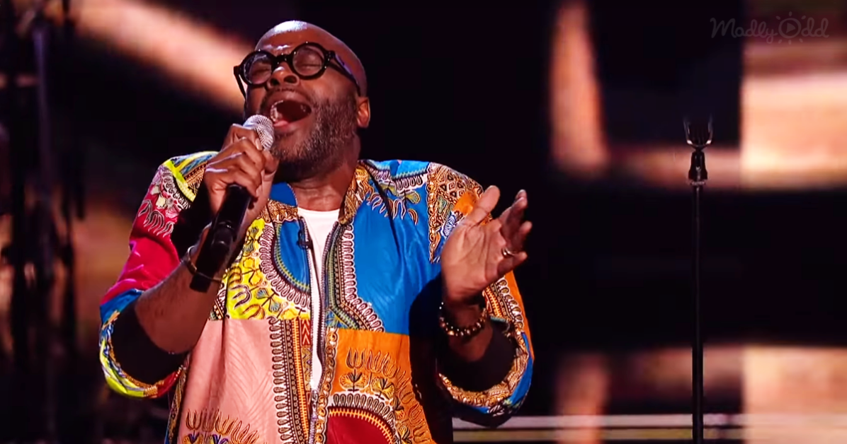 A man in a vibrant, patterned shirt sings passionately into a microphone on stage.