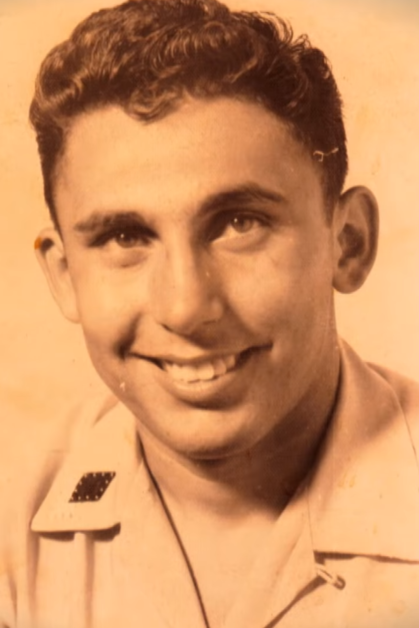 A smiling man with short, curly hair, wearing a light-colored shirt, is the main subject of this vintage photo.