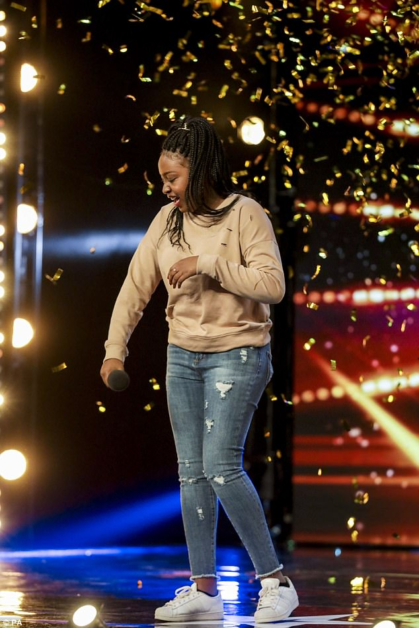 A person in a beige sweatshirt and jeans walks on a stage with confetti falling around them.
