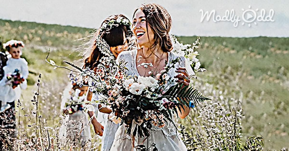 A bride in a 150-year-old handmade wedding dress is walking through a field, holding a bouquet.