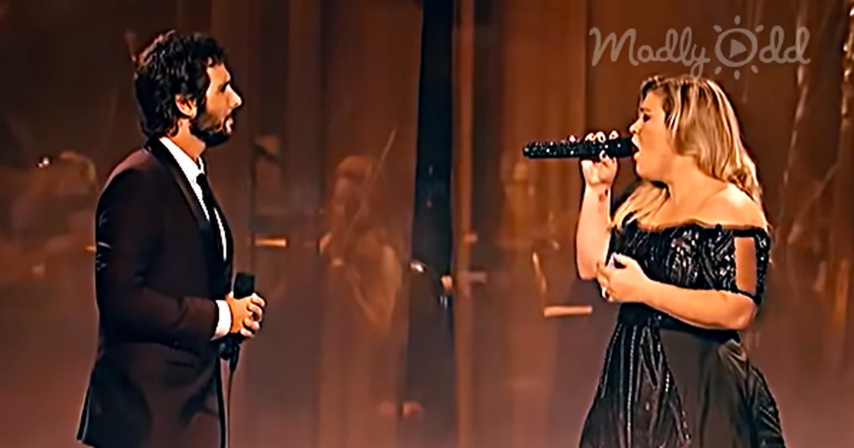 A man in a suit and a woman in a black dress perform on stage, captivating an audience with their rendition of "The...