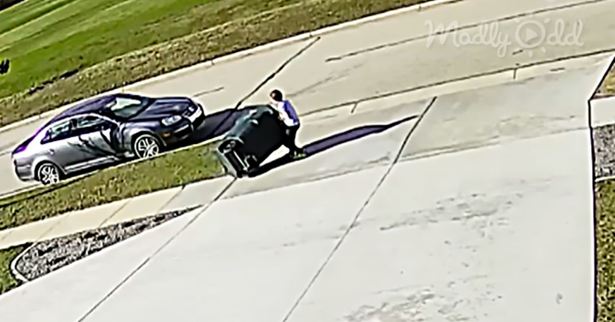 A little boy is seen battling a garbage bin on a sidewalk, with a car nearby.