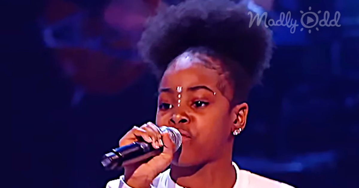 A young rapper in a white jacket with rainbow stripes performs on stage, holding a microphone.