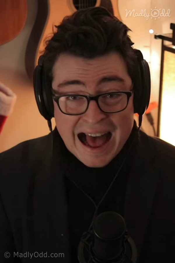 A person wearing headphones and a black turtleneck is singing or speaking into a microphone.