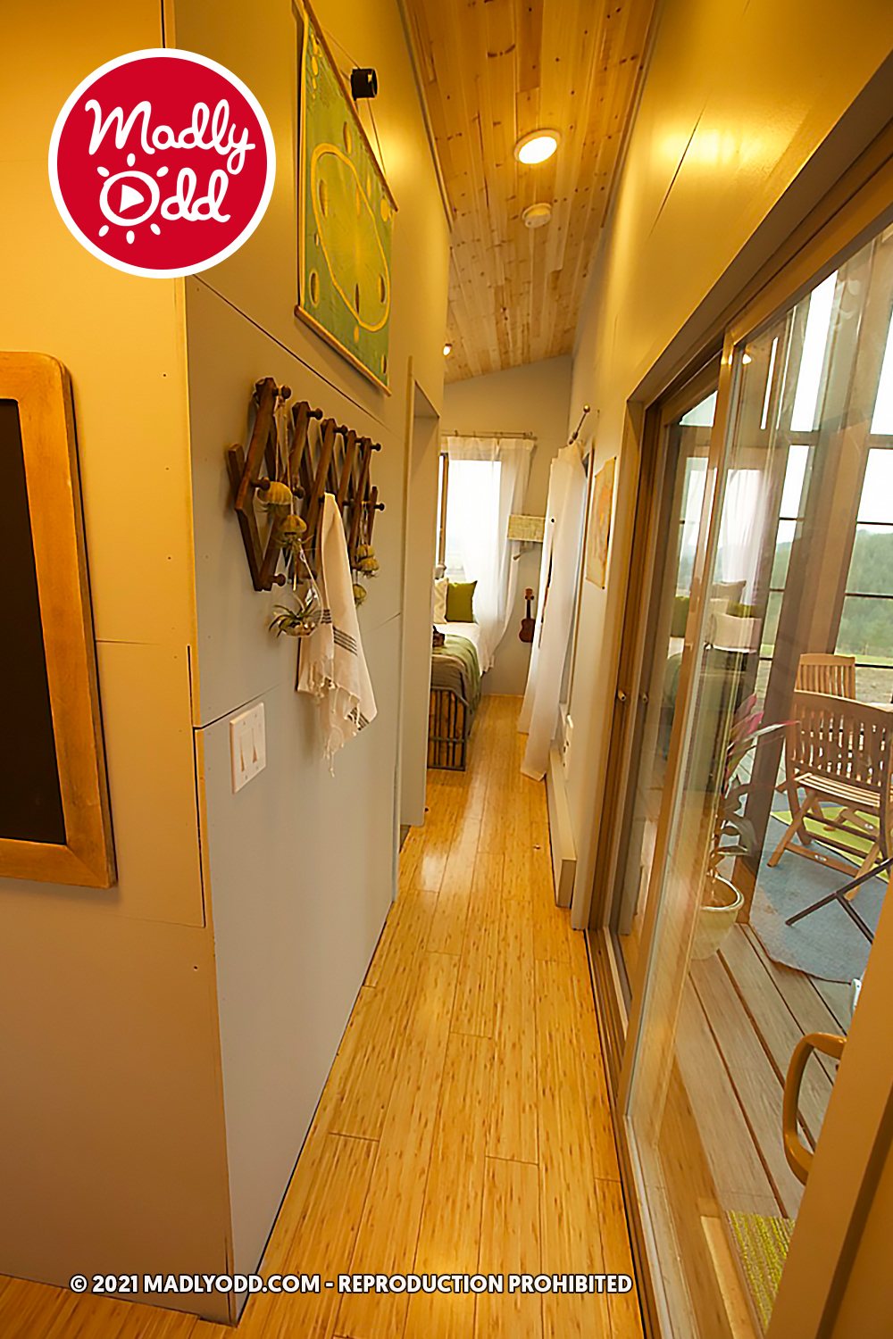 A narrow hallway with wooden floors, a sliding glass door, and a bed in the background.