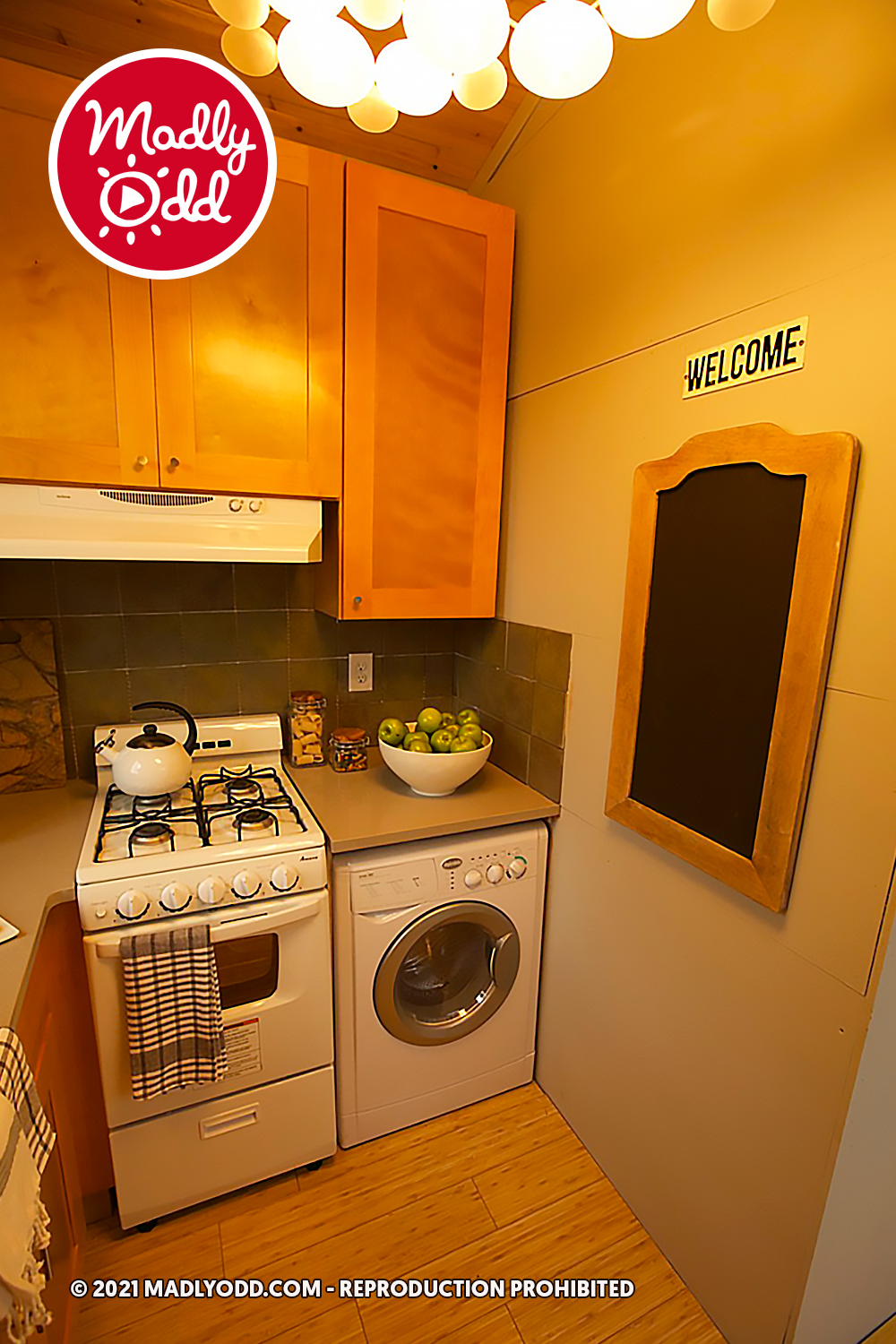 A cozy kitchen corner with a stove, washer, and a bowl of apples on the counter.