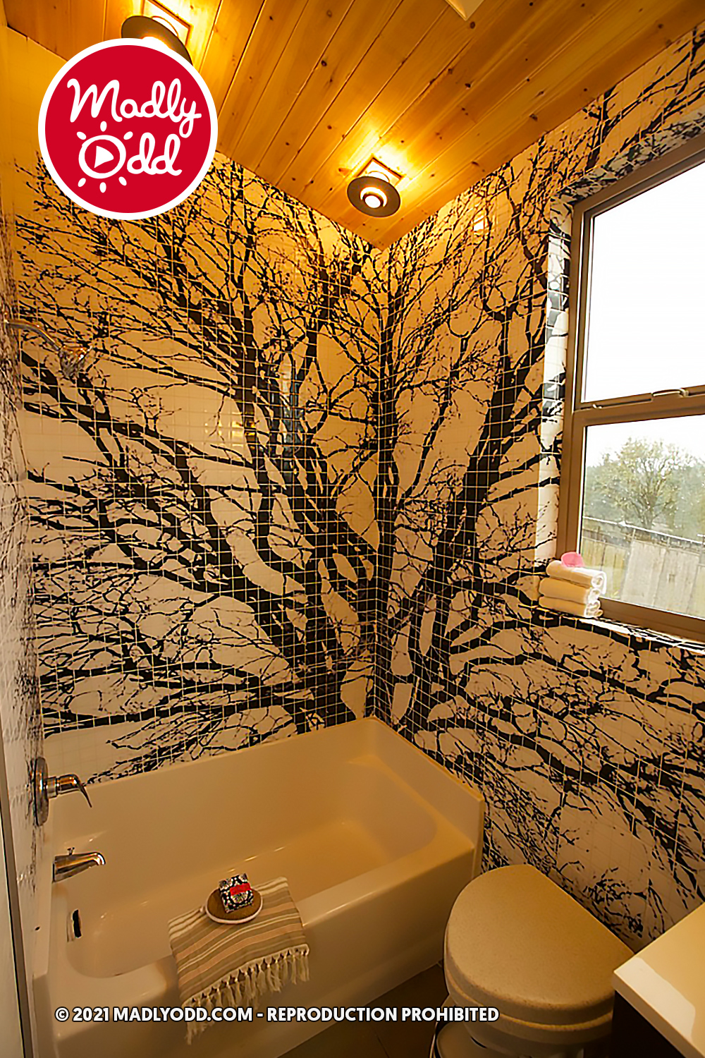 A bathroom with a bathtub, toilet, and wall tiles featuring a tree design.